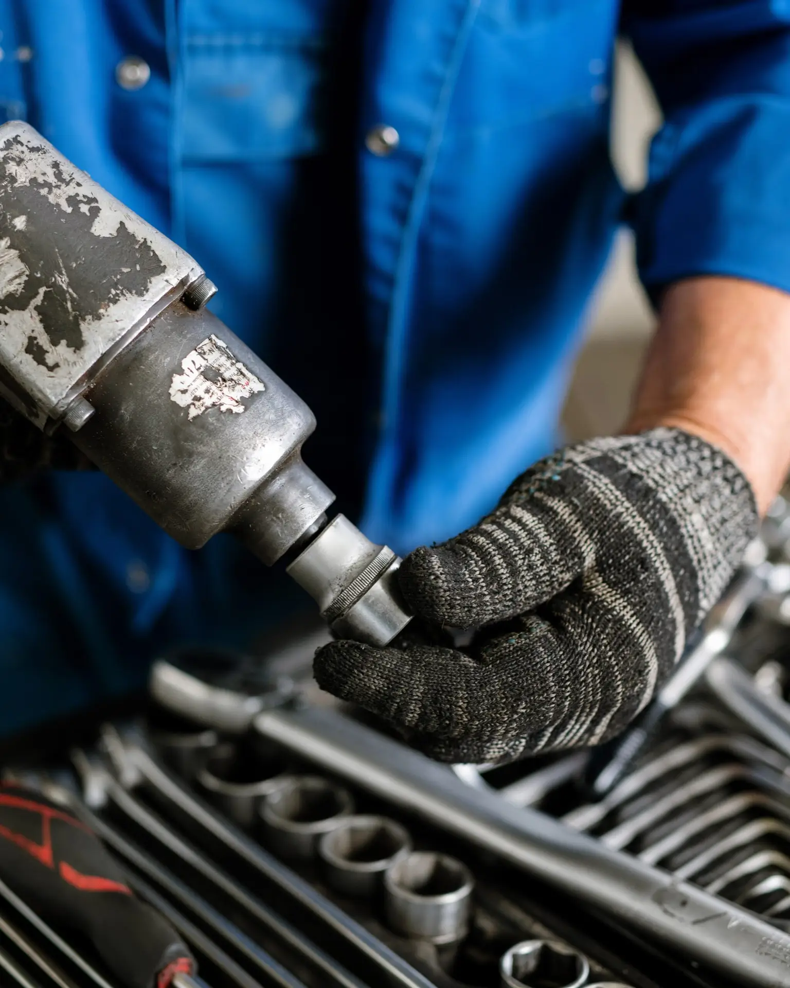 Gloved mechanic or repairman in workwear putting one of nozzles on metallic drill before carrying out repair work